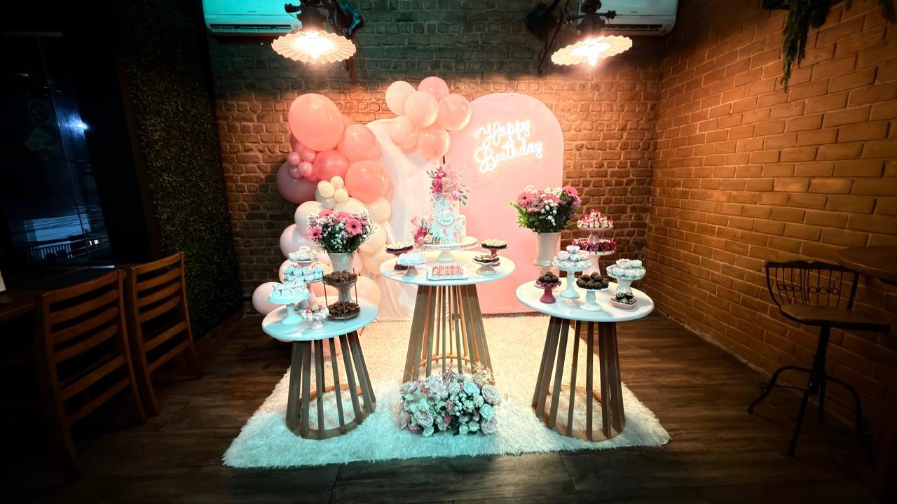 Mesa de aniversário no Vitral, com arco de balões rosa, bolo e letreiro Happy Birthday.