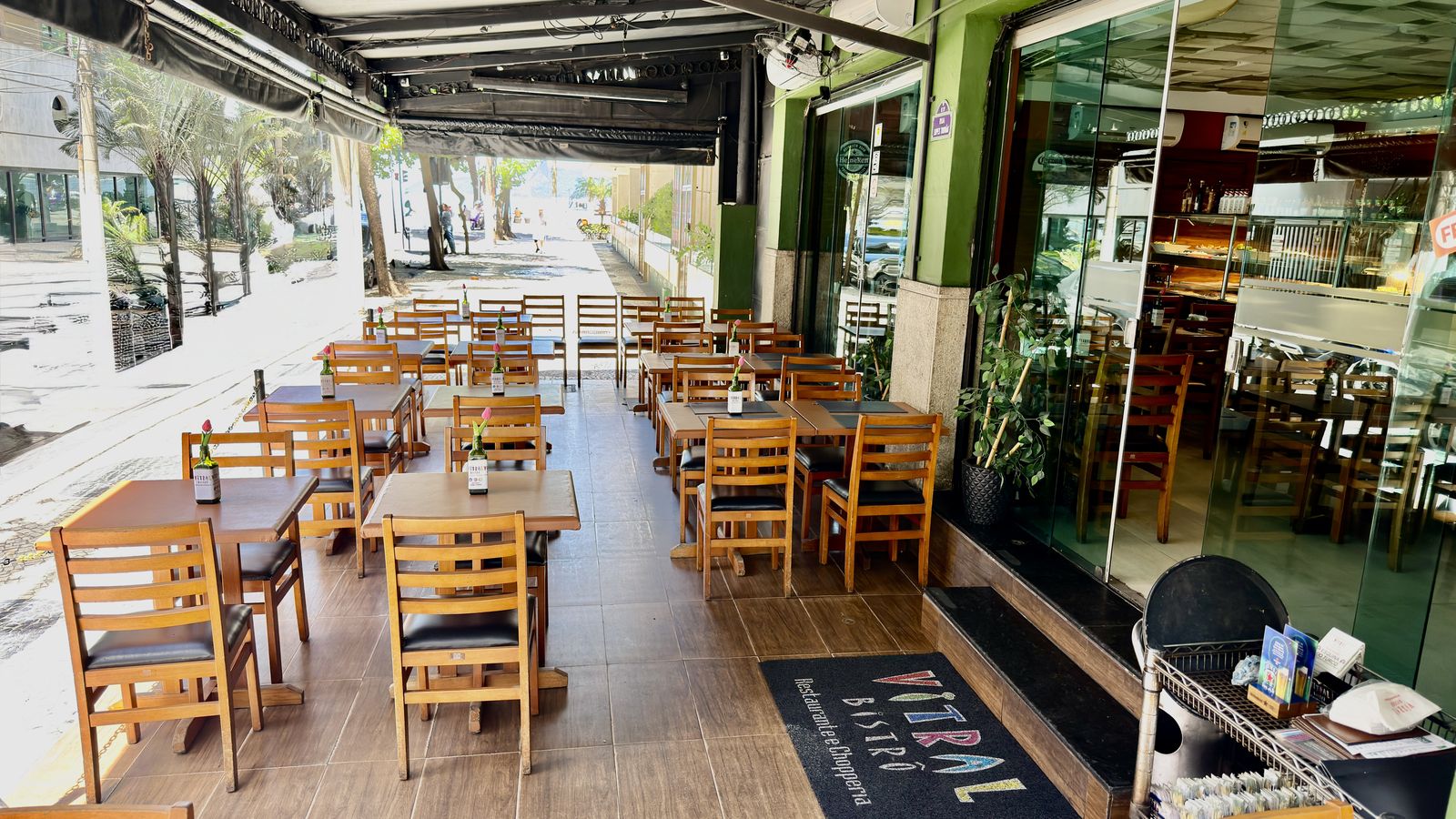 Calçada do Vitral Bistrô, com mesas de madeira e a fachada de vidro.