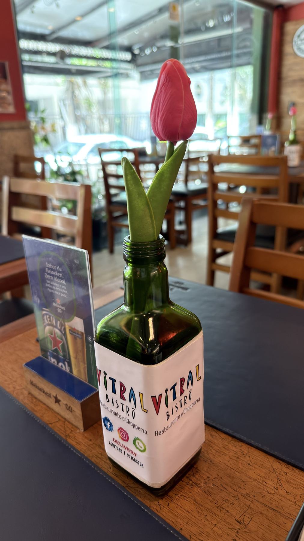 Tulipa rosa em uma garrafa verde com o rótulo do Vitral Bistrô.